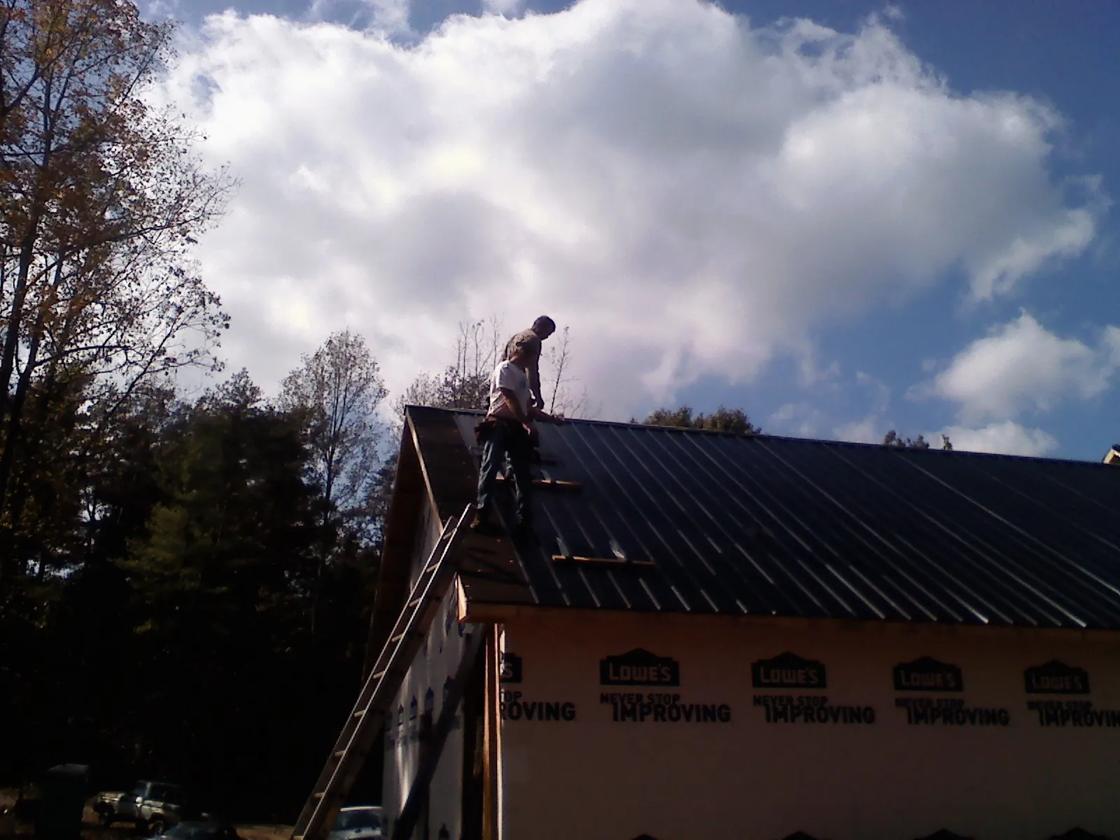 Roofer fastening dark metal panels high against a cloudy sky, from a Roof Inspection job in Camp Verde