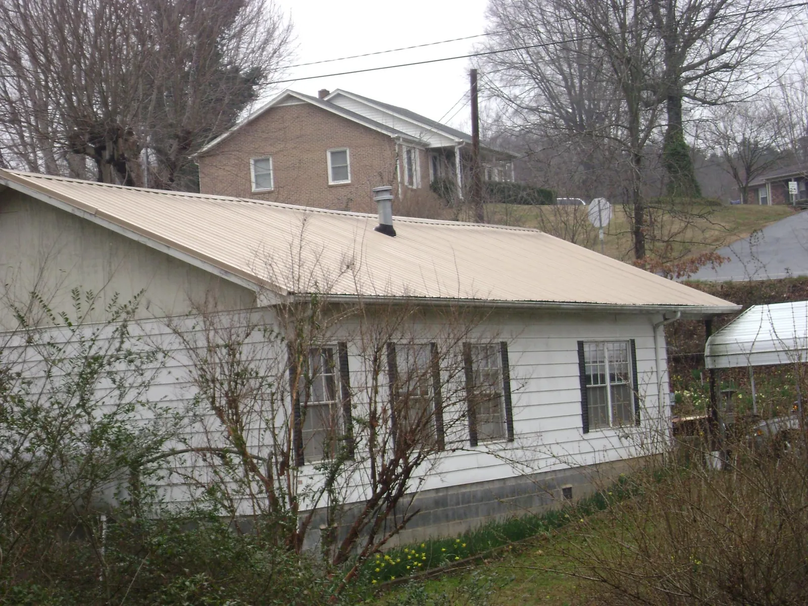 Tan metal roof on a white sided house set into a hillside — Commercial Roofing by Roofing Brothers in Camp Verde